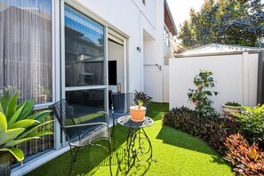 A patio with a table and chairs, a potted plant, and a small garden area with various plants.