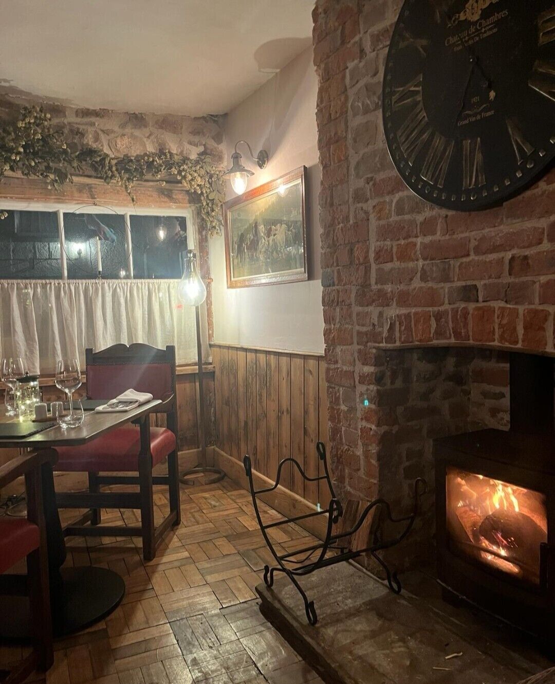 A cozy dining area with a brick wall, a fireplace, a clock, and a window with curtains.