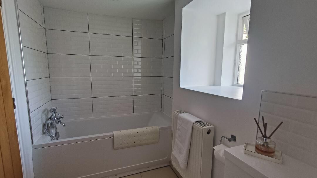 Et badeværelse med badekar, bøjler til håndklæder, en radiator og et vindue.