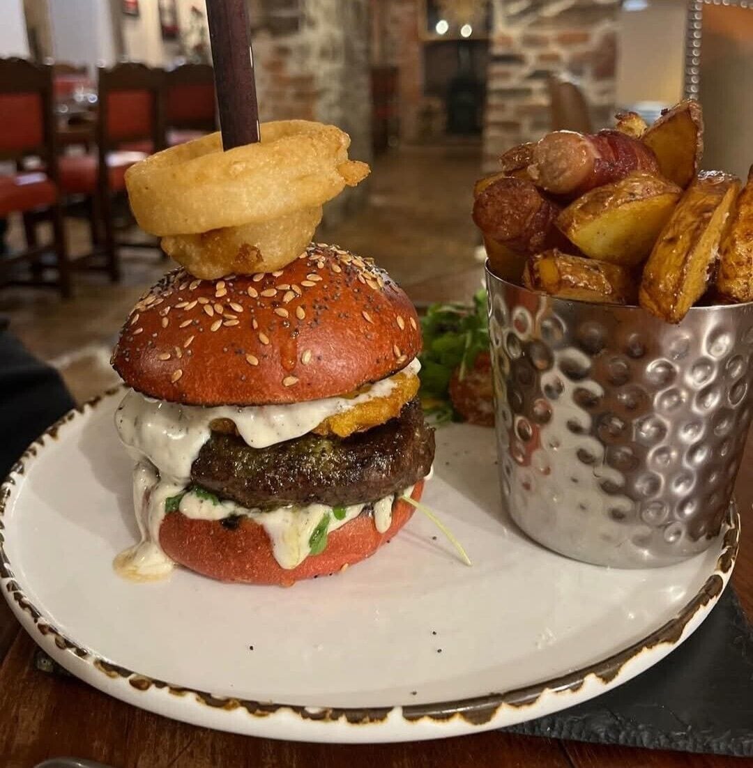 Hamburguesa con pan de sésamo, una carne, salsa cremosa y una guarnición de papas fritas crujientes en un recipiente metálico.