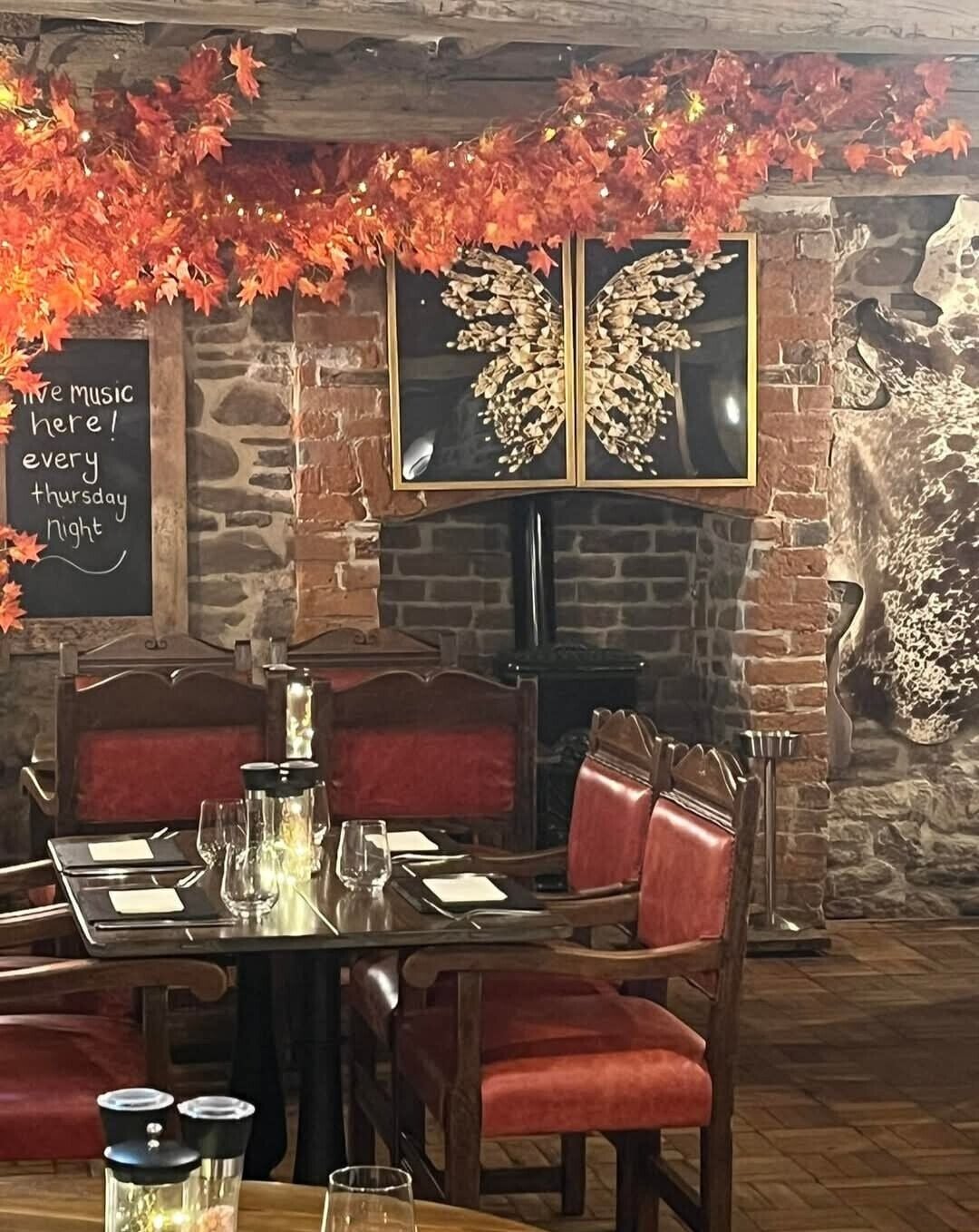 Een restaurantinterieur met een bakstenen muur, een open haard, een eettafel gedekt voor twee personen en decoraties met herfstthema.