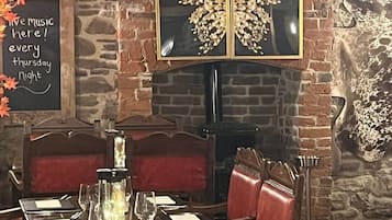 Een restaurantinterieur met een bakstenen muur, een open haard, een eettafel gedekt voor twee personen en decoraties met herfstthema.