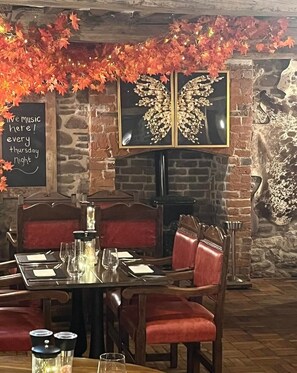 A restaurant interior with a brick wall, a fireplace, a dining table set for two, and autumn-themed decorations.