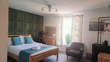 Ein Schlafzimmer mit einem Bett, einem Sessel, einer Kommode, einem Spiegel und einem Fenster mit Vorhängen.