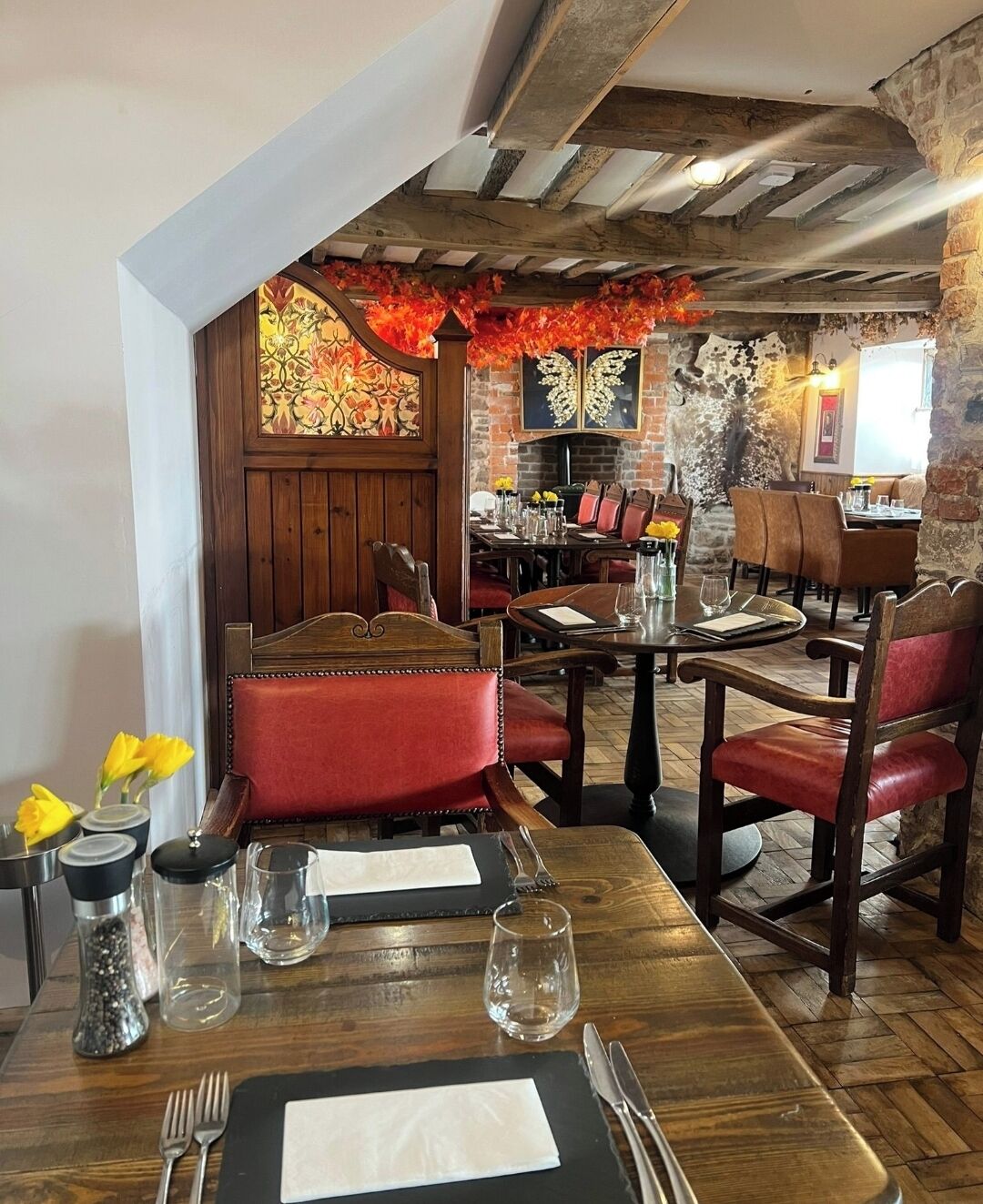 A restaurant interior with wooden tables, red upholstered chairs, and a brick wall.