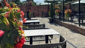 Un área de patio al aire libre con mesas y sillas, luces colgantes y plantas en macetas.