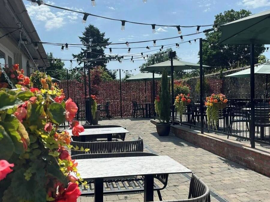 An outdoor patio area with tables and chairs, string lights overhead, and potted plants.