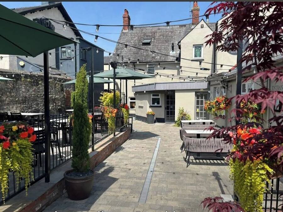 An outdoor patio area with tables and chairs, surrounded by buildings and potted plants.
