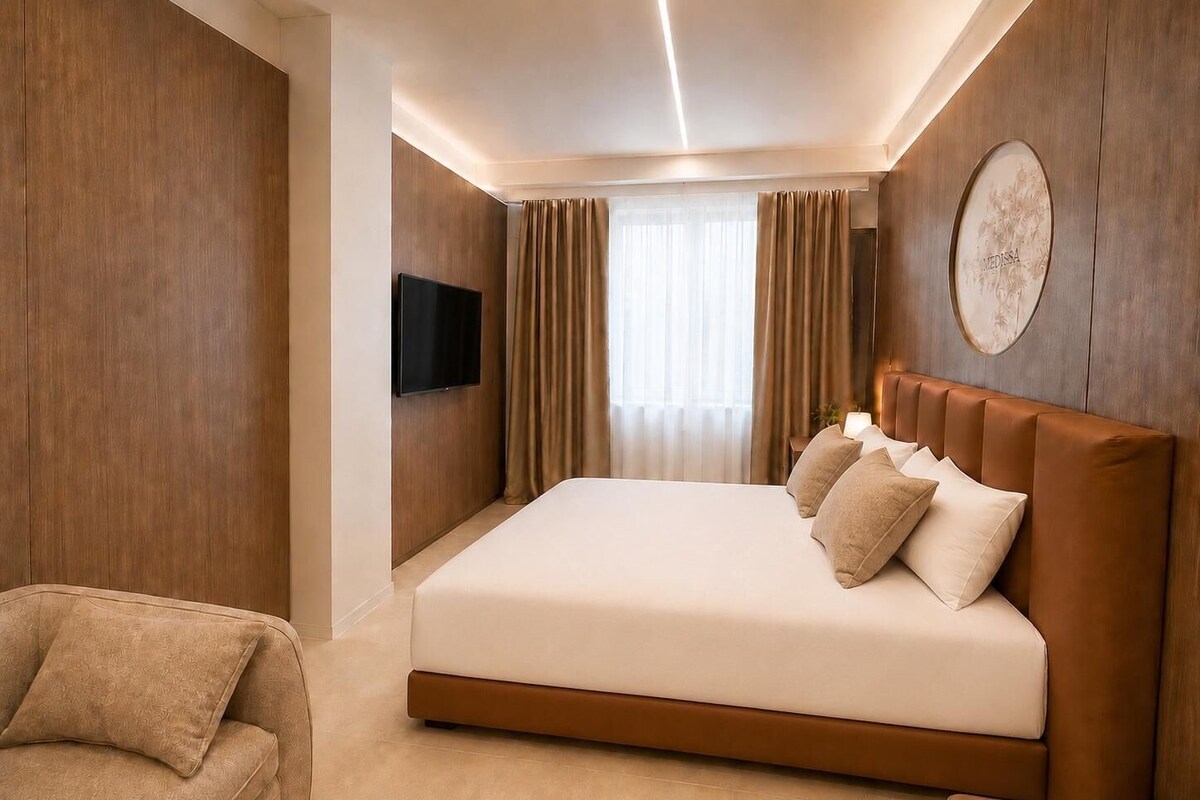 A hotel room with a large bed, a flat-screen TV mounted on the wall, and a sofa.