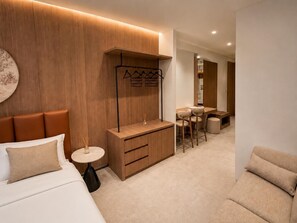 Une chambre d’hôtel moderne comprenant un lit, une petite table ronde, un meuble en bois, un coin salon avec une table et des chaises, et un porte-manteau.