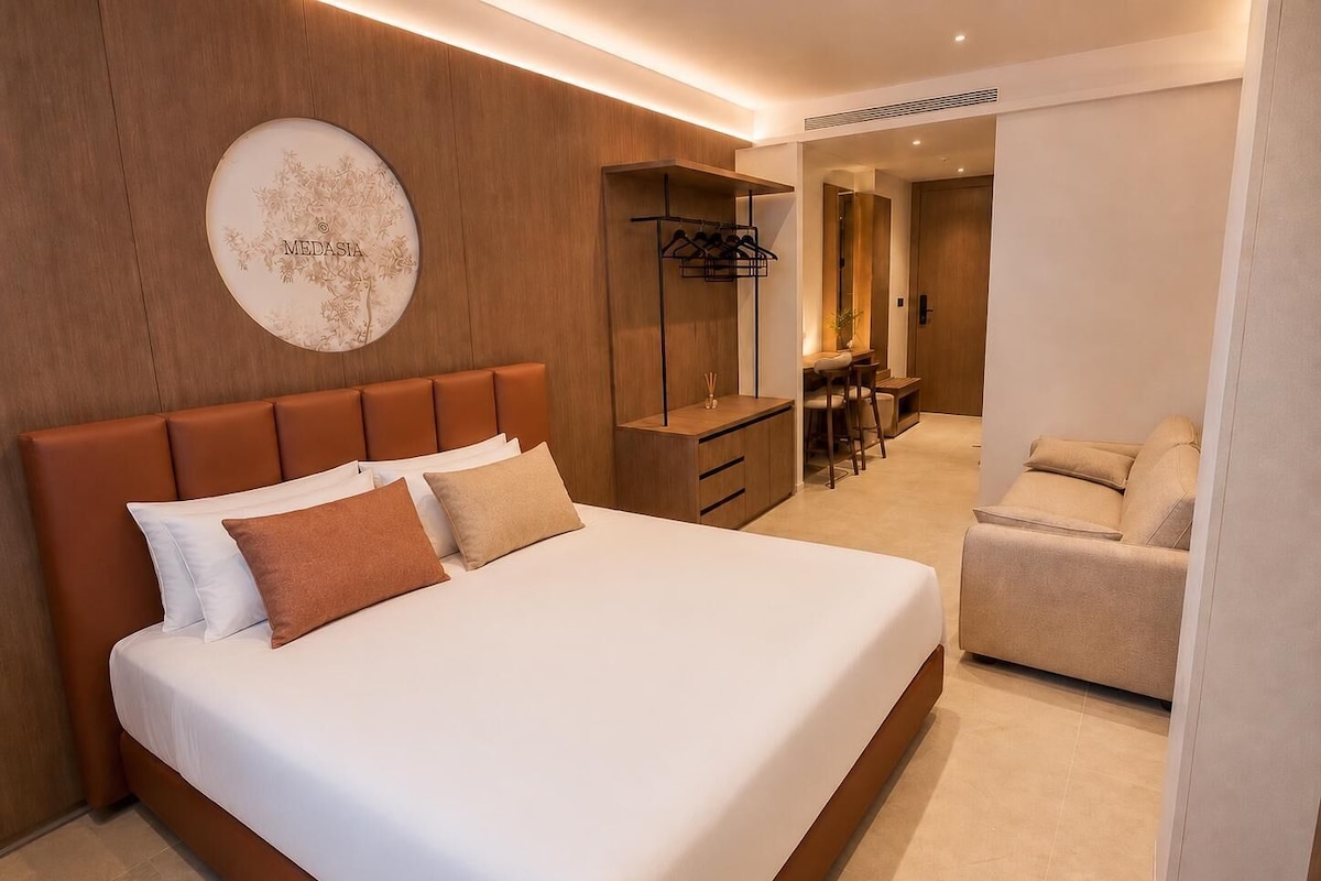A modern hotel room with a large bed, a desk, and a seating area.