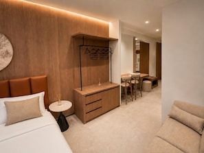 A modern hotel room with a bed, a small round table, a wooden cabinet, a seating area with a table and chairs, and a coat rack.