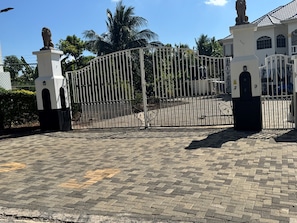 A gated entrance with a lion statue, paved walkway, and a building with arched windows.