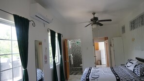 A bedroom with a bed, a ceiling fan, a window with curtains, and a door leading to a bathroom. - TheBreeze2022 — Comfort, Style & Everything You Need for the Perfect Stay (Clarendon Park)