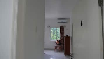 Ein Flur mit einer Tür, auf der die Zahl '6' steht, der zu einem Zimmer mit Fenster, Stuhl und kleinem Tisch führt.