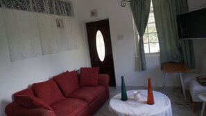 A living room with a red sofa, a round table with vases, a door with a stained glass window, and a television on a stand. - TheBreeze2022 — Comfort, Style & Everything You Need for the Perfect Stay (Clarendon Park)