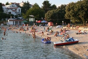 A beach with people swimming and sunbathing, a lifeguard tower, and a row of beach umbrellas. - Schöne Ferienwohnung "Scampi" in ruhigem Stadtteil von Pula mit 2 Schlafzimmer (Pula)