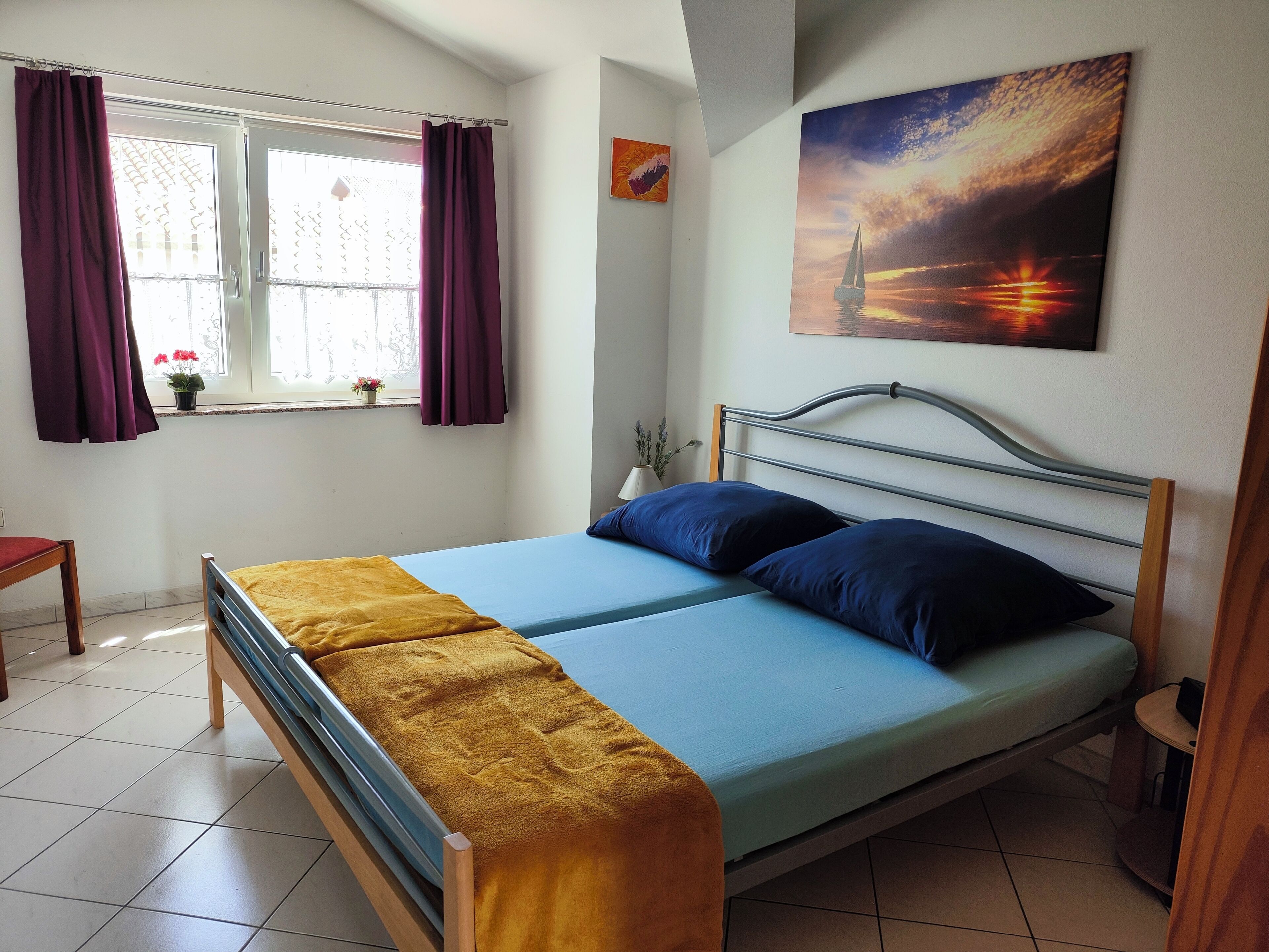 A bedroom with a bed, curtains, a window with a view, a painting, and a small table.