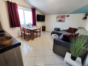 A cozy living room with a dining area, a flat-screen TV mounted on the wall, and a large window with curtains. - Schöne Ferienwohnung "Scampi" in ruhigem Stadtteil von Pula mit 2 Schlafzimmer (Pula)