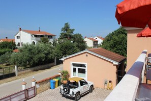 A residential area with a white car parked in front of a house with a red roof. There is a small building with a number '10' on it, and a red umbrella is visible in the foreground. - Schöne Ferienwohnung "Scampi" in ruhigem Stadtteil von Pula mit 2 Schlafzimmer (Pula)