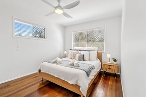 A bedroom with a bed, a ceiling fan, a bedside table with a lamp, and a window with blinds.