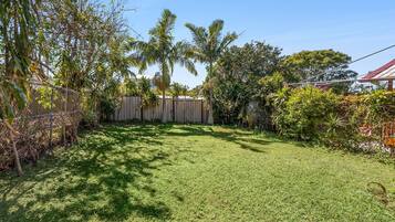 A backyard with a wooden fence, a grassy lawn, and various trees and shrubs.