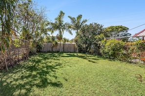 A backyard with a wooden fence, a grassy lawn, and various trees and shrubs.