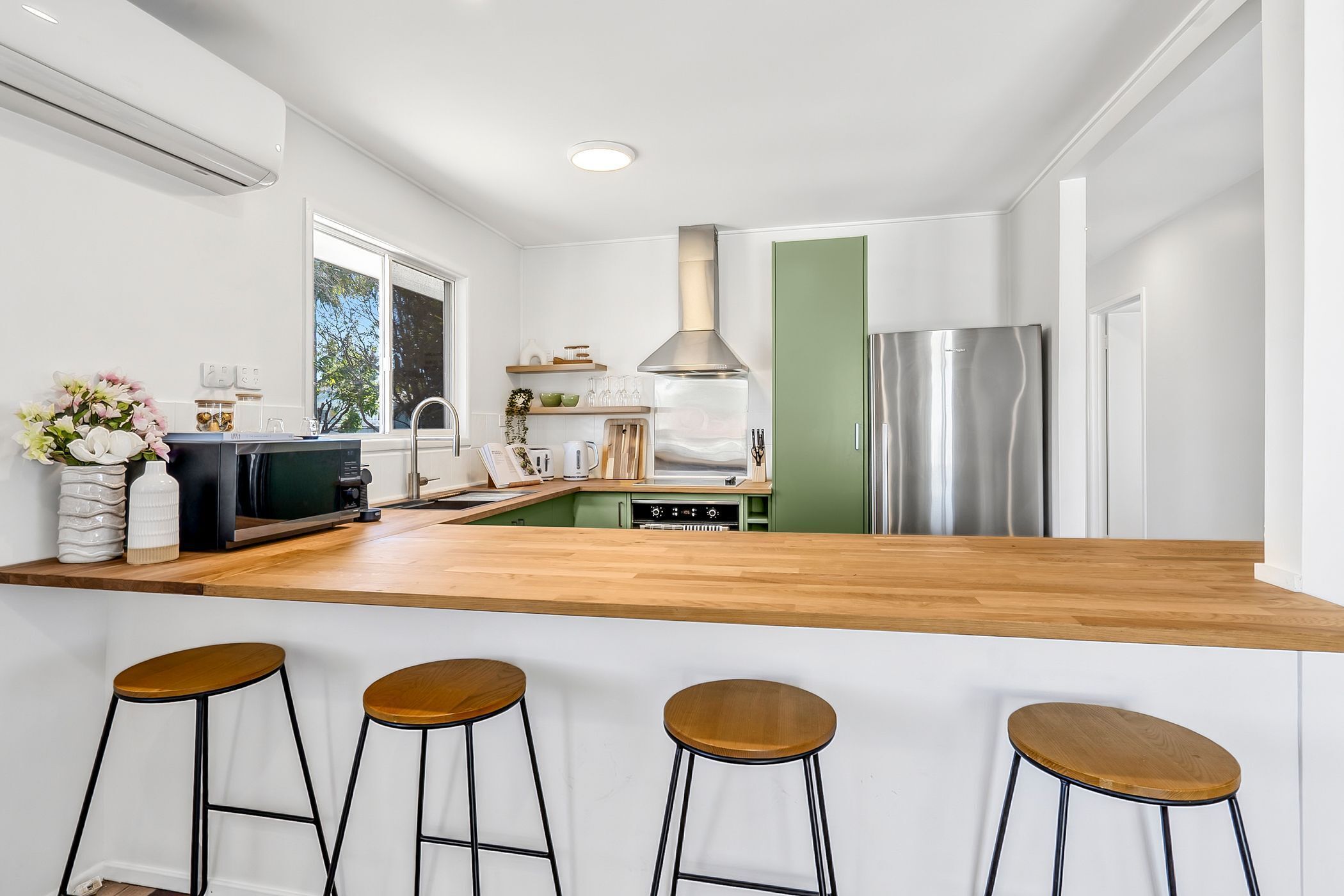A modern kitchen with a wooden countertop, stainless steel appliances, and bar stools.