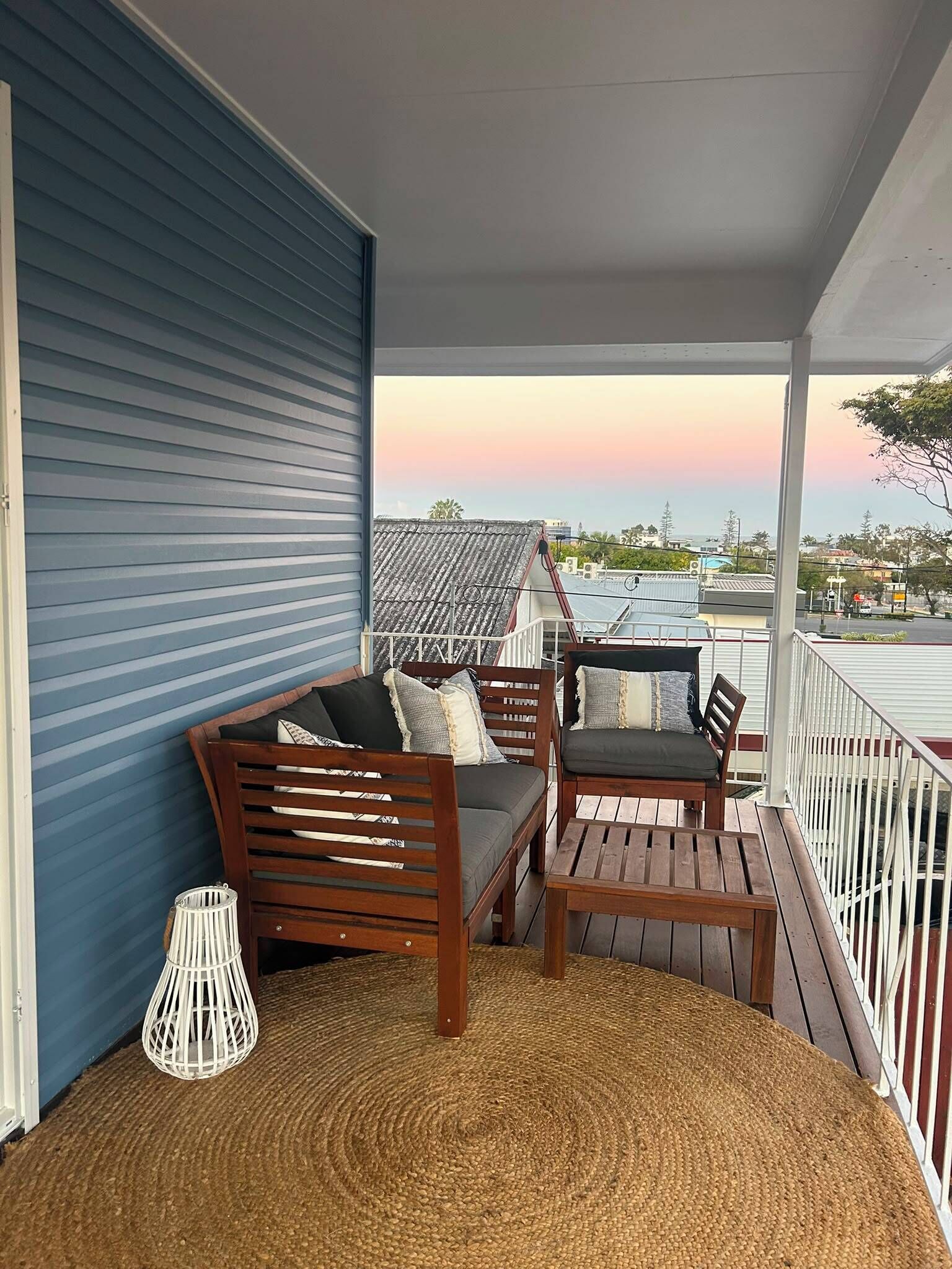 A covered porch with a blue wall, a wooden bench, a small table, and a wicker lamp.