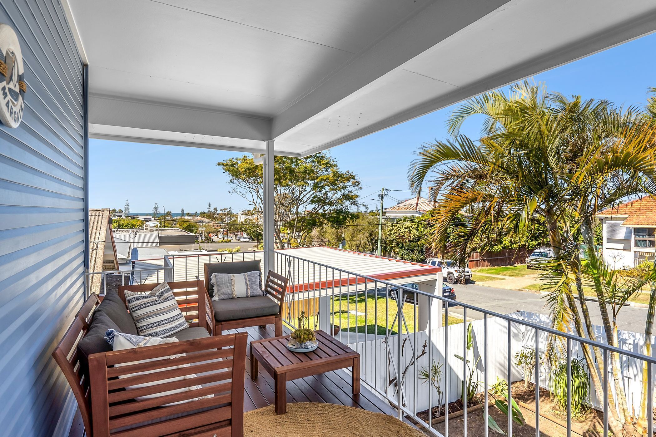 A balcony with wooden furniture, a view of the street, and a clear sky.