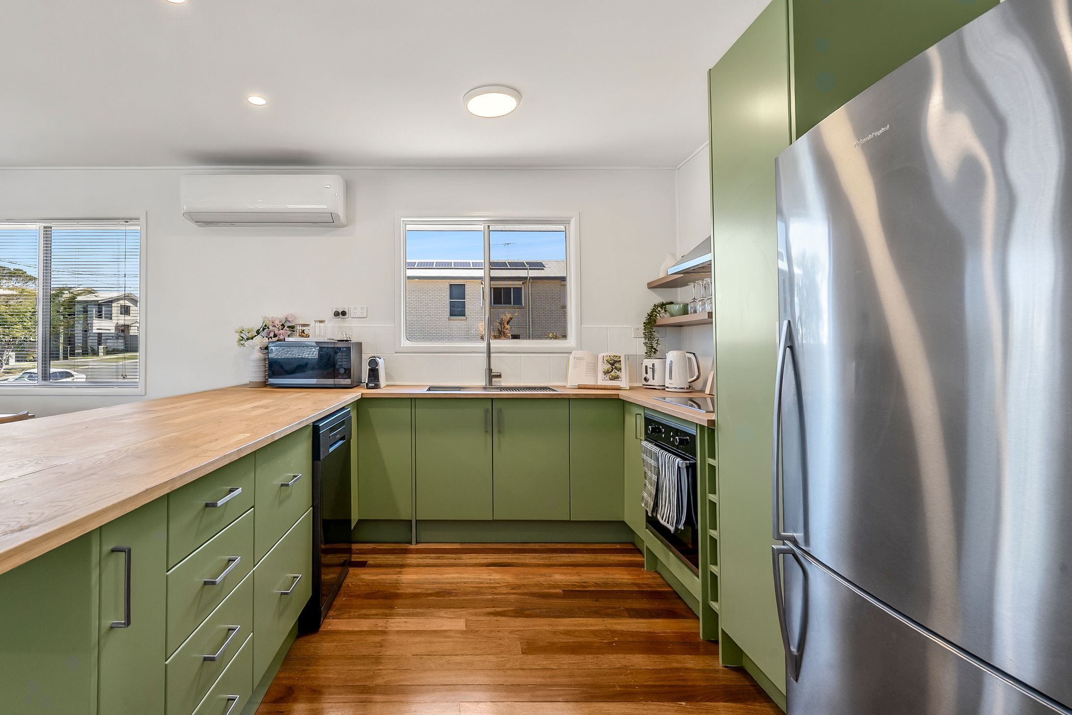 A modern kitchen with green cabinets, a stainless steel refrigerator, and a wooden countertop.