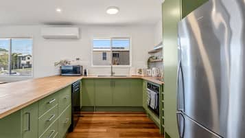A modern kitchen with green cabinets, a stainless steel refrigerator, and a wooden countertop.