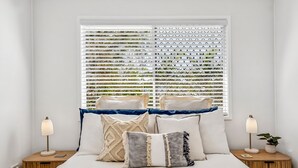 Un dormitorio con cama, almohadas, mesitas de noche, lámparas y una ventana con persianas.