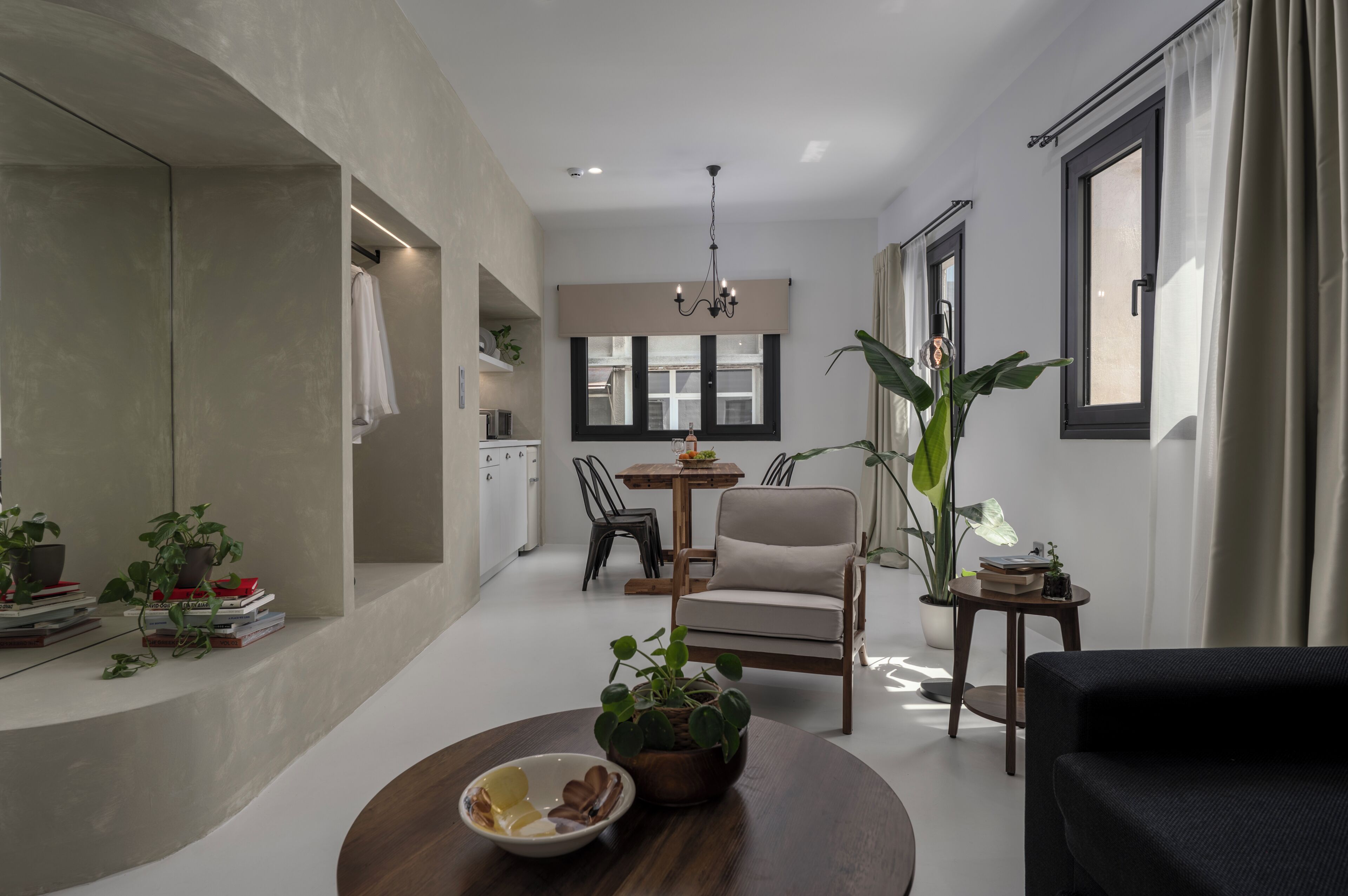 Un salon moderne avec un coin repas, une cuisine à l’arrière-plan et une grande fenêtre avec des rideaux.
