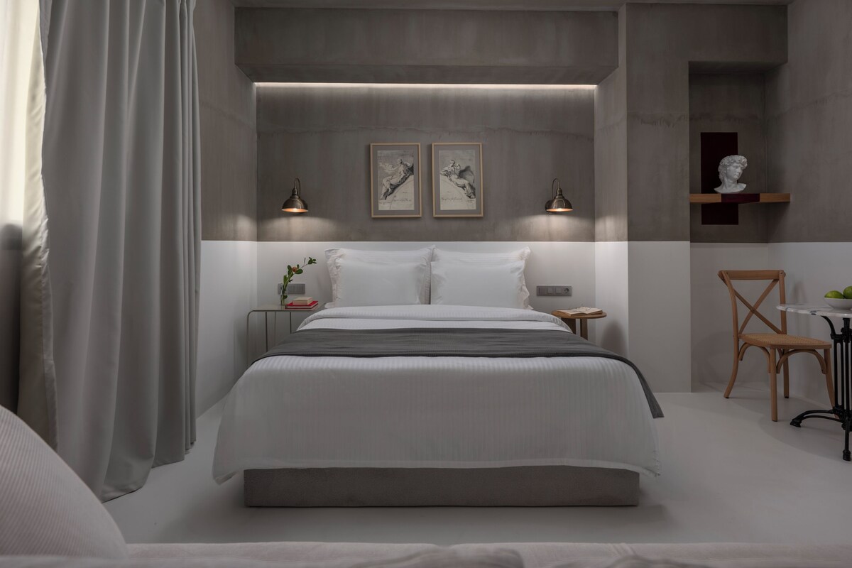 A modern bedroom with a large bed, bedside tables, a chair, and artwork on the wall.