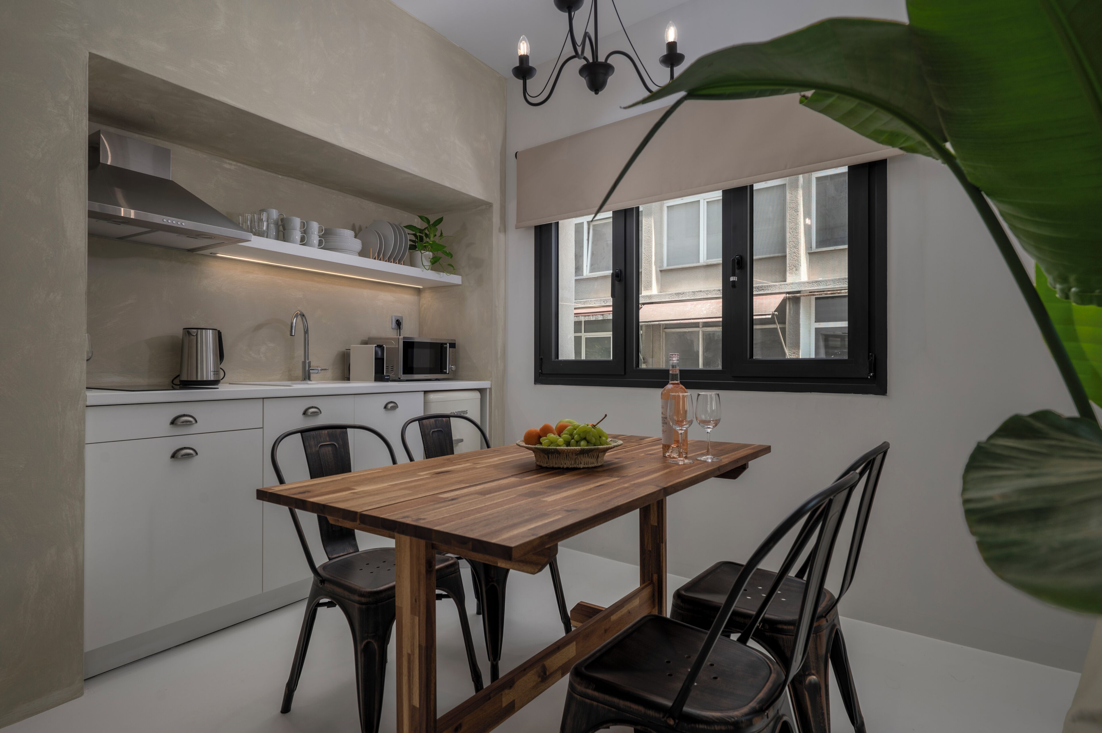 A compact kitchen with white cabinets, a wooden dining table, and a window with black shutters.