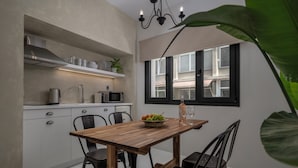 A compact kitchen with white cabinets, a wooden dining table, and a window with black shutters. - Binome Suites (Thessaloniki)