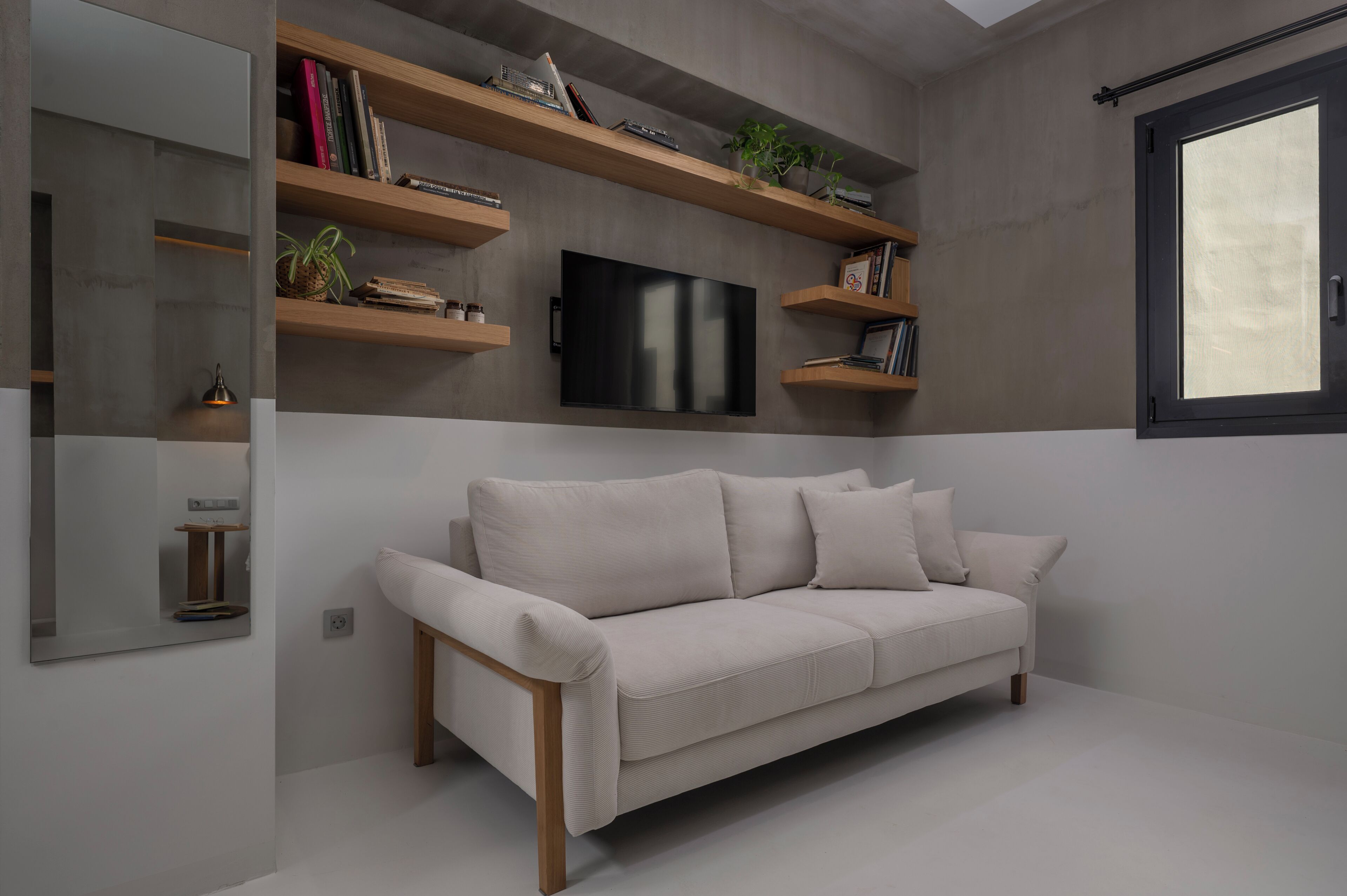 A modern living room with a sofa, built-in shelves, a flat-screen TV, and a large window.