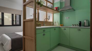 Une cuisine compacte avec des meubles de couleur verte, une cloison en bois et une fenêtre avec des stores.