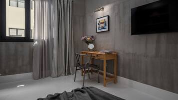 A bedroom with a bed, a desk with a chair, a TV on the wall, and a window with curtains.