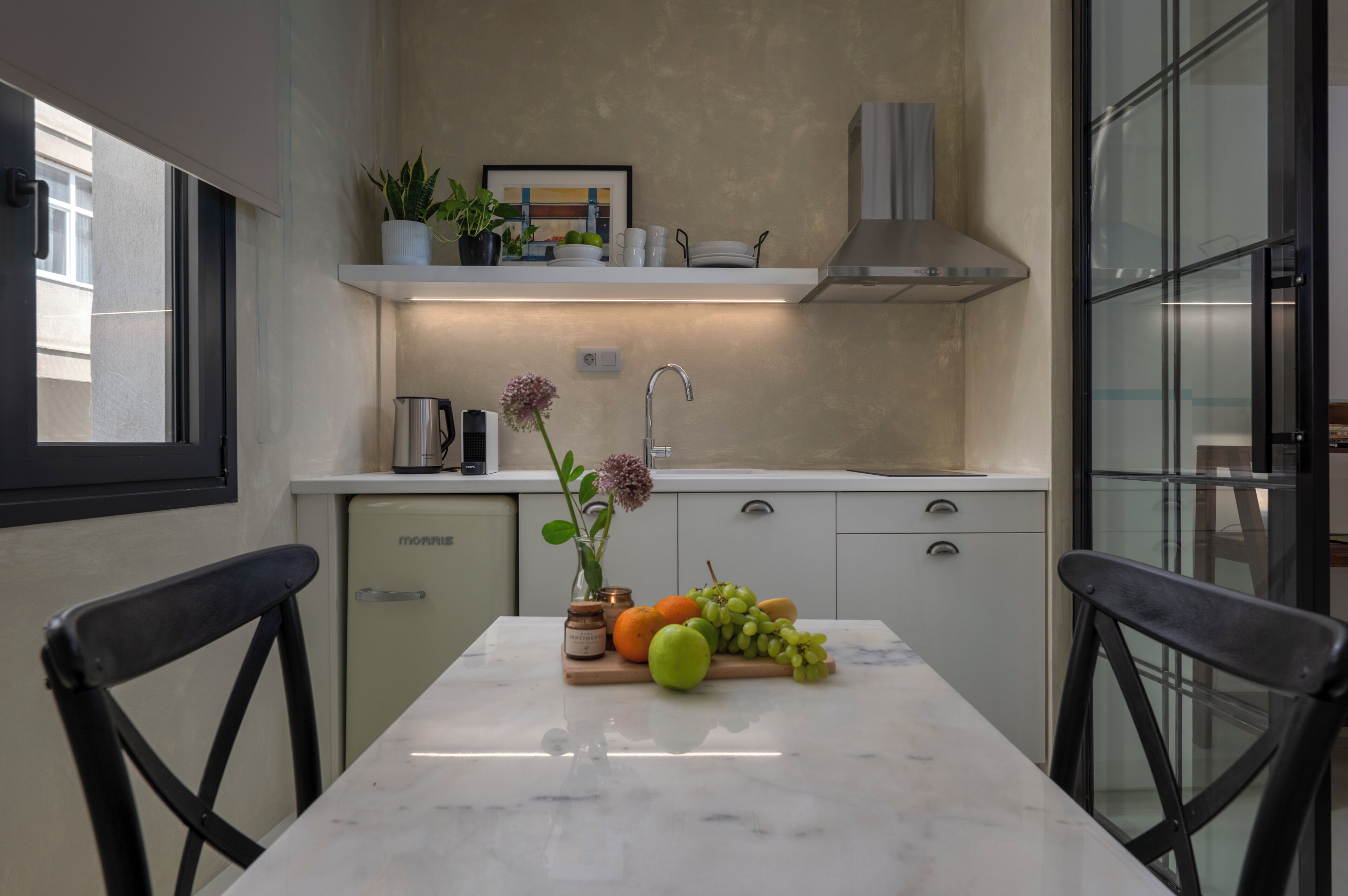 A modern kitchen with a marble countertop, a refrigerator, and a dining area with two chairs.