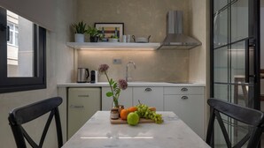 A modern kitchen with a marble countertop, a refrigerator, and a dining area with two chairs. - Binome Suites (Thessaloniki)