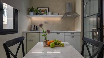A modern kitchen with a marble countertop, a refrigerator, and a dining area with two chairs.