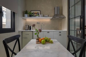 A modern kitchen with a marble countertop, a refrigerator, and a dining area with two chairs. - Binome Suites (Thessaloniki)