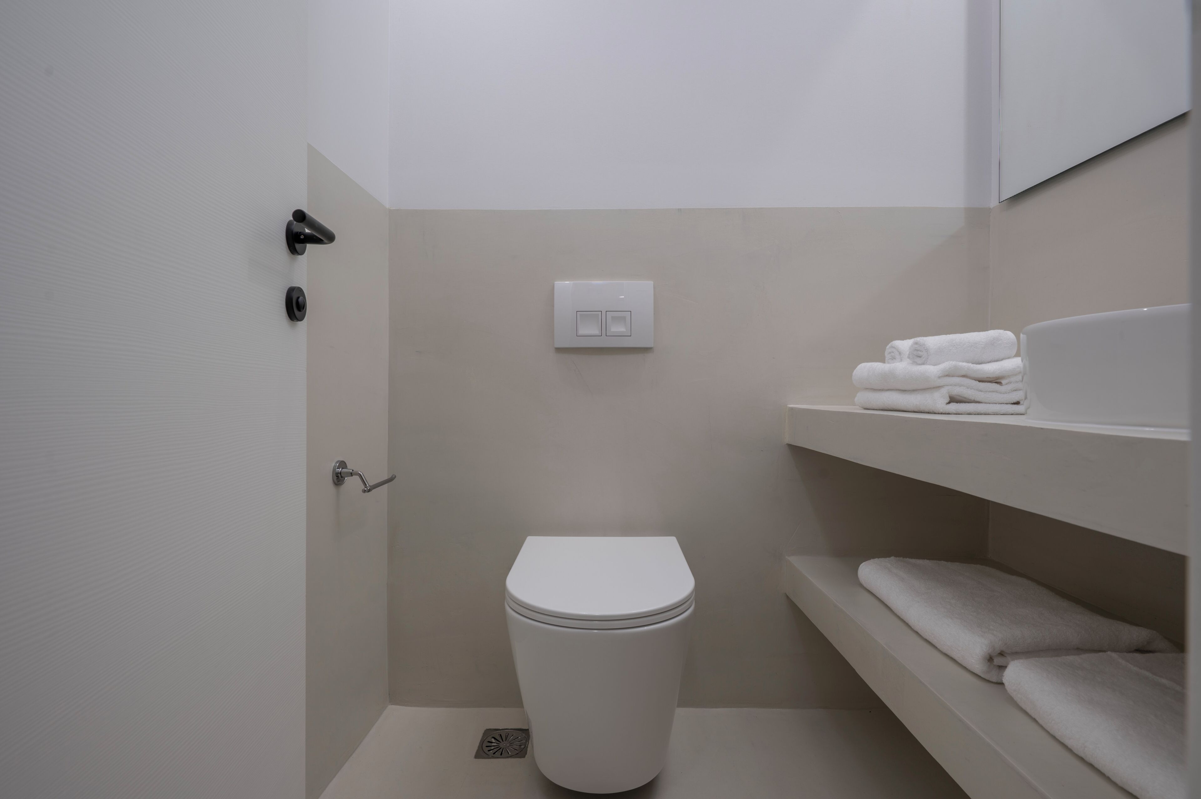 A small, modern bathroom with a toilet, a towel rack, and a shelf with folded towels.
