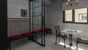 A modern interior with a glass partition, red cushioned seating, a table with chairs, and a chandelier. - Binome Suites (Thessaloniki)