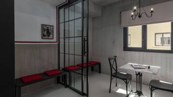 A modern interior with a glass partition, red cushioned seating, a table with chairs, and a chandelier.