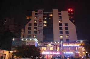 Un hotel con un letrero llamativo que indica 'Hotel Maam Residency' y un cartel publicitario que anuncia 'Vibes of India'.