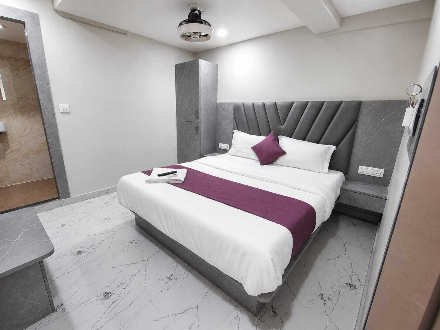 Una habitación de hotel moderna con cama, mesita de noche, armario empotrado y ventilador de techo.