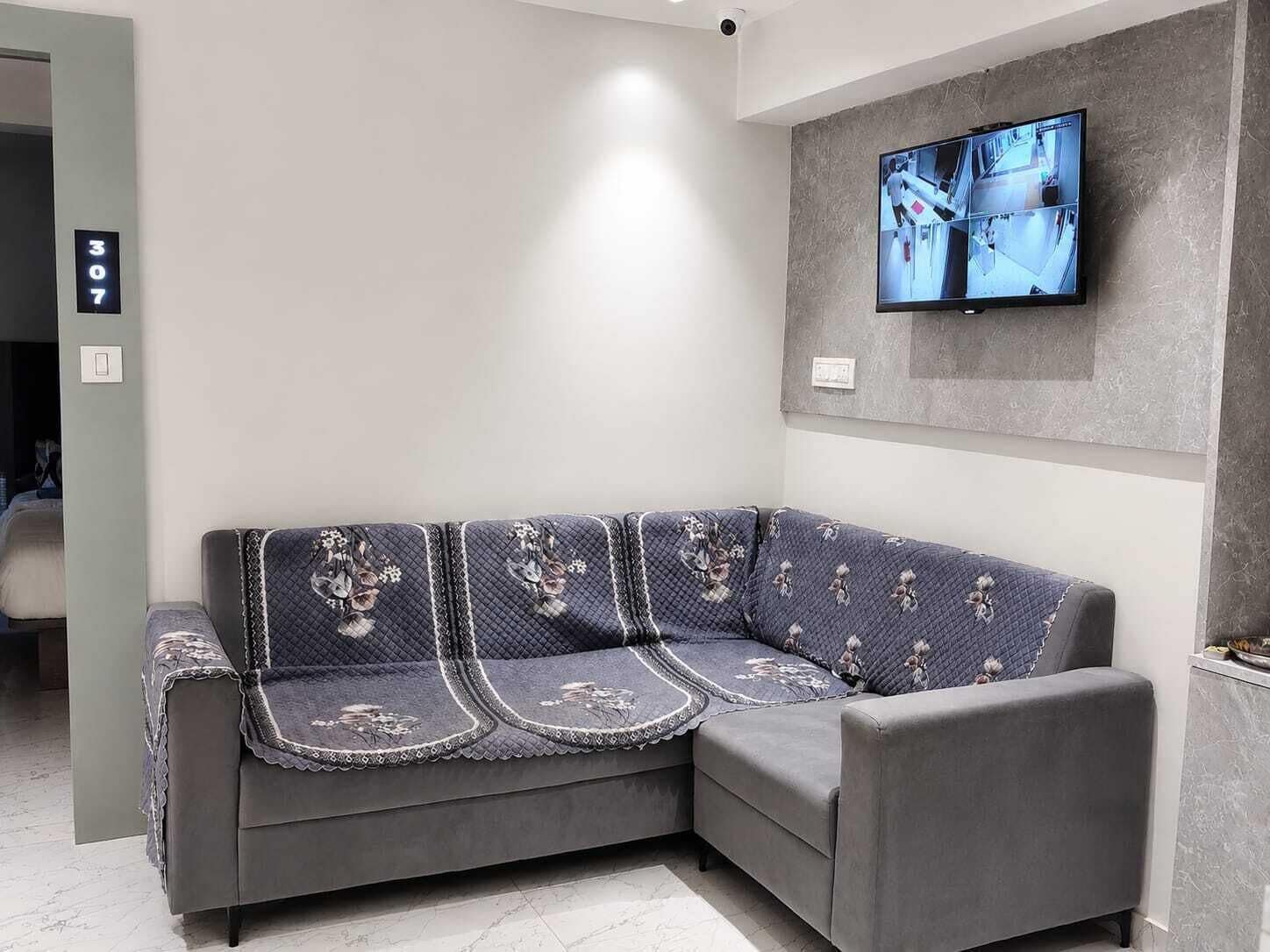 Ein graues Sofa mit floralem Bezug in einem modernen Zimmer, in dem ein an der Wand befestigtes Fernsehgerät einen Sicherheitsüberblick zeigt.